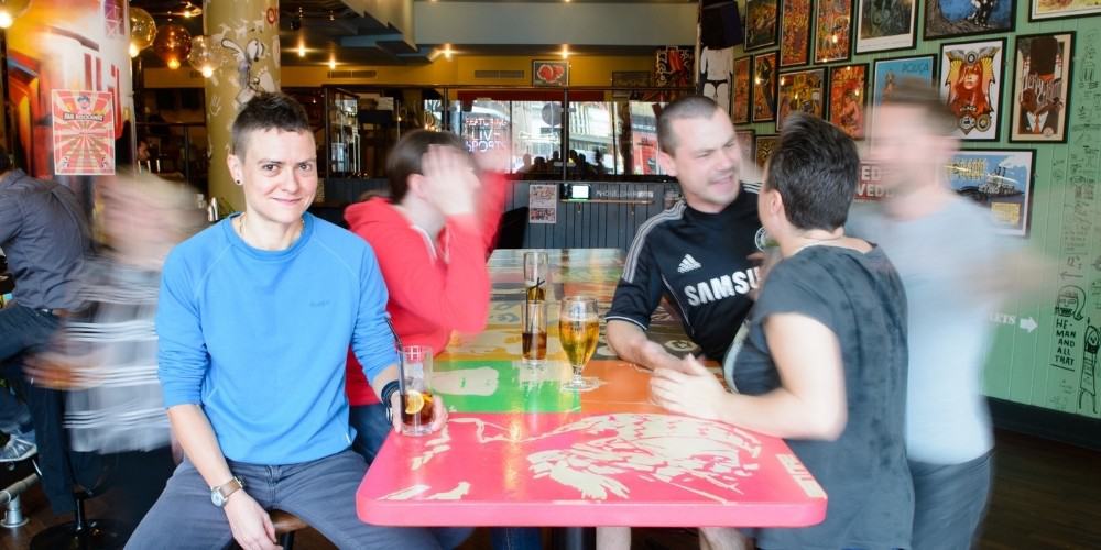 Do you lose friends when you quit drinking? Person sitting quietly in a bar surrounded by activity.