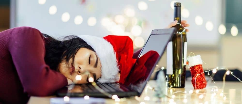 Image: Woman in Santa hat asleep on her laptop holding a bottle of wine. How can I drink less this Christmas?